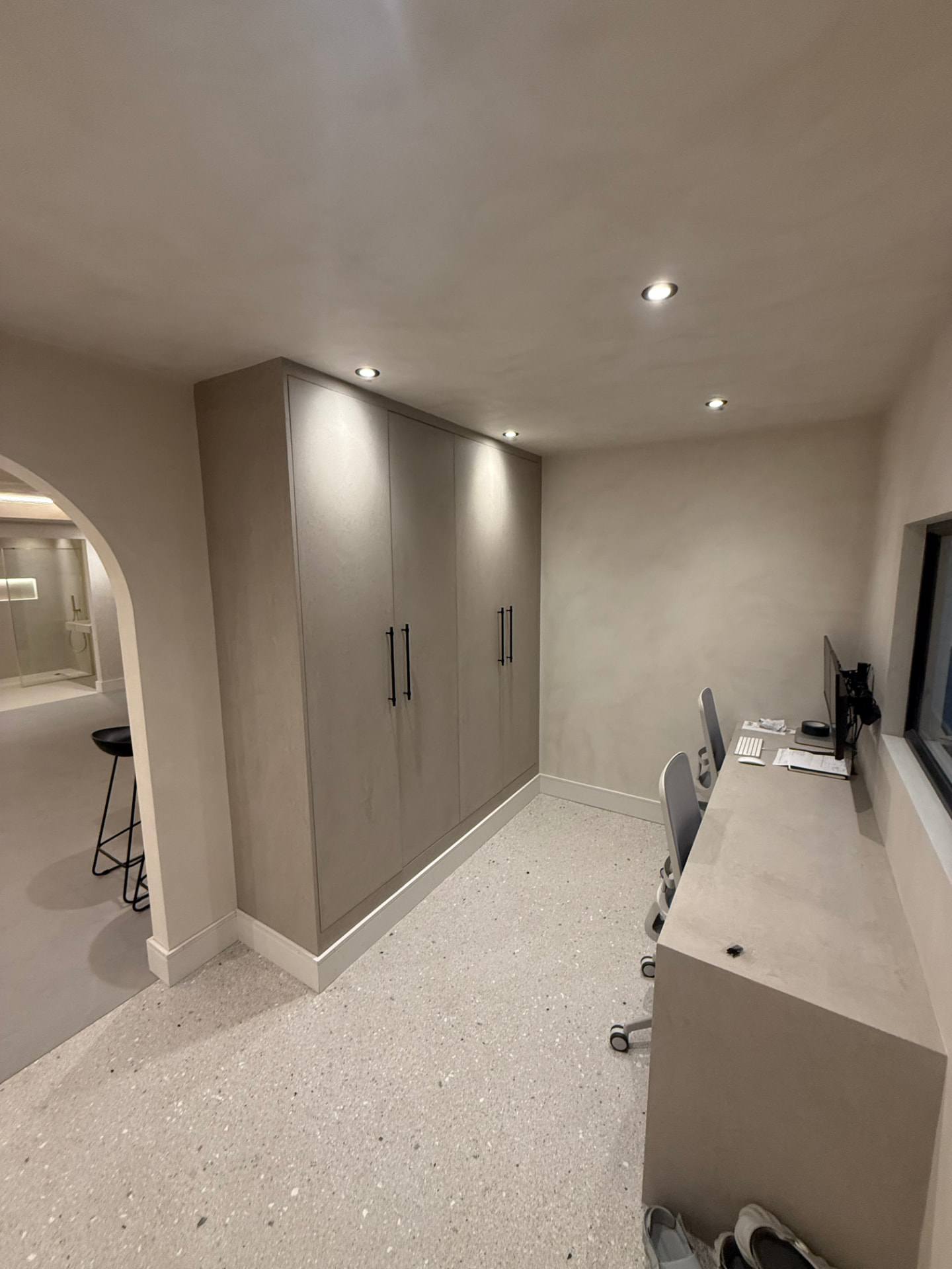 Floor-to-ceiling taupe wardrobe with black bar handles beside a built-in desk